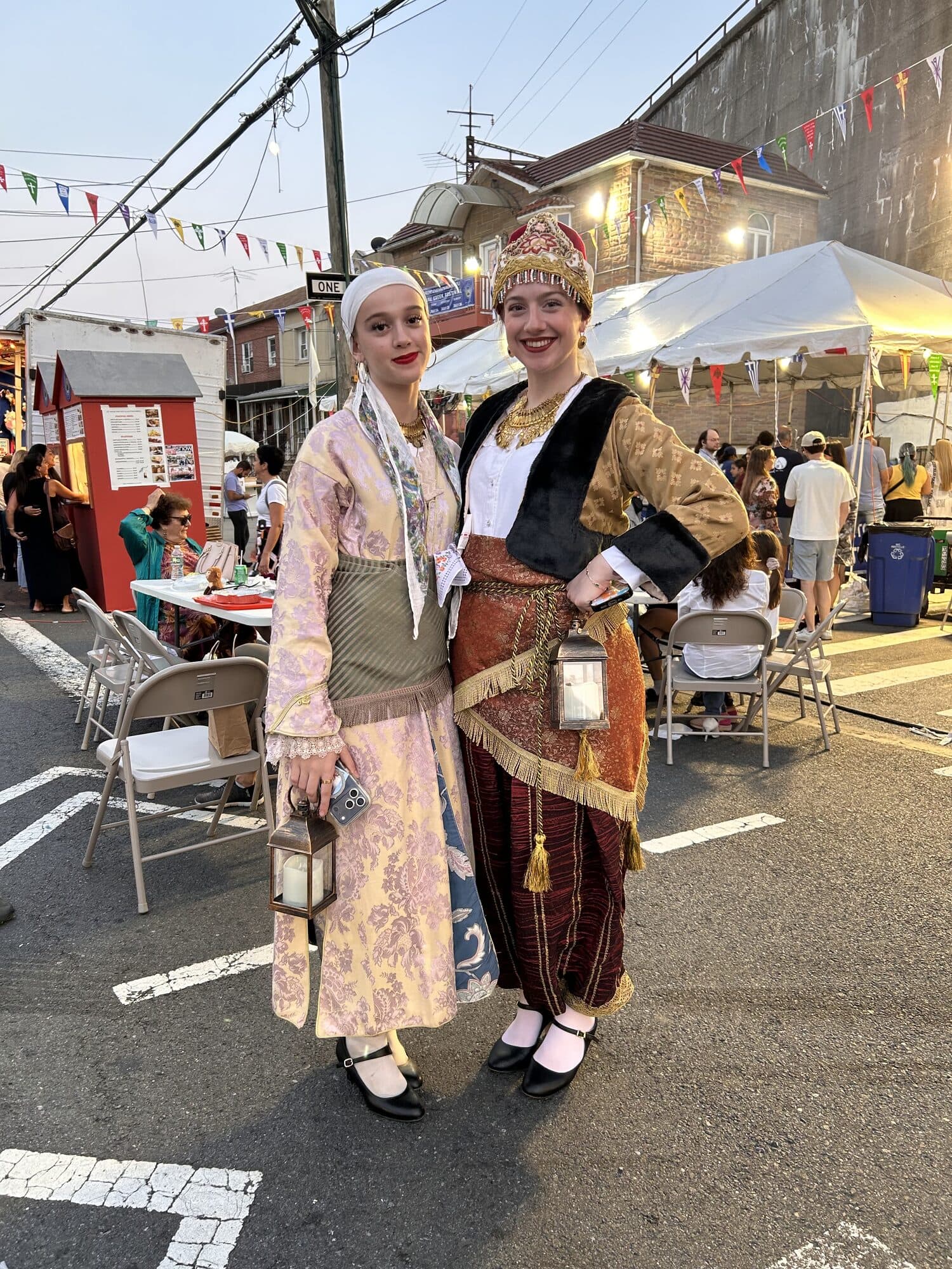 Two members of the folk dance troupe in embroidered regional costume, carrying lanterns